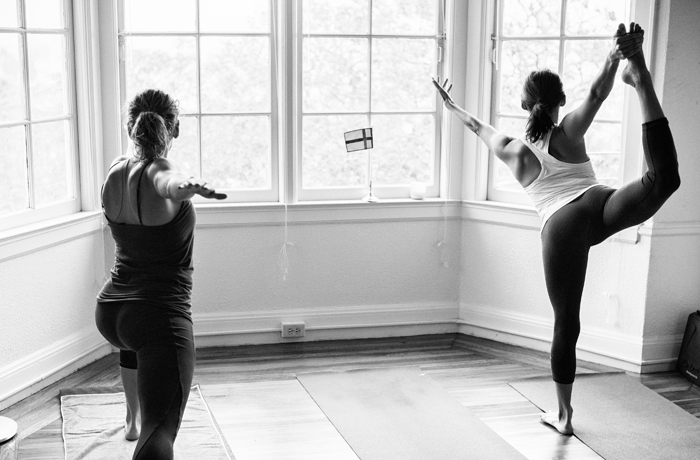 A imagem mostra duas mulheres praticando yoga dentro de casa