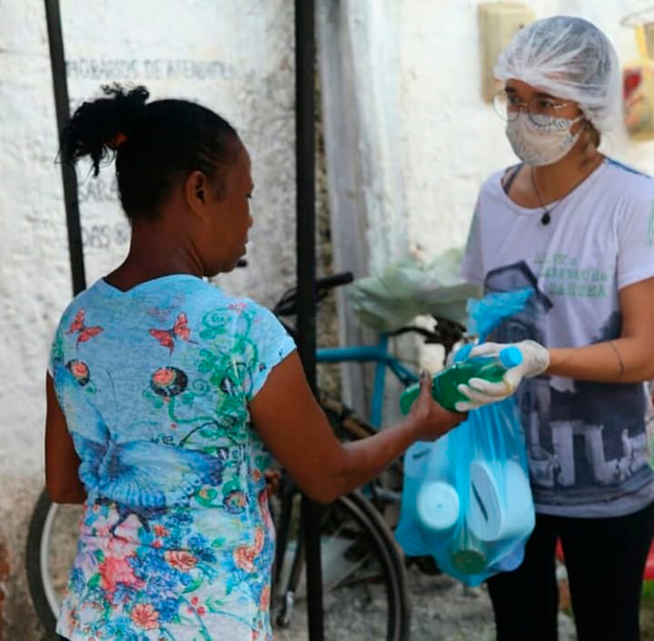 Voluntária entrega doações para uma mulher em ação do projeto Várzea Viva.