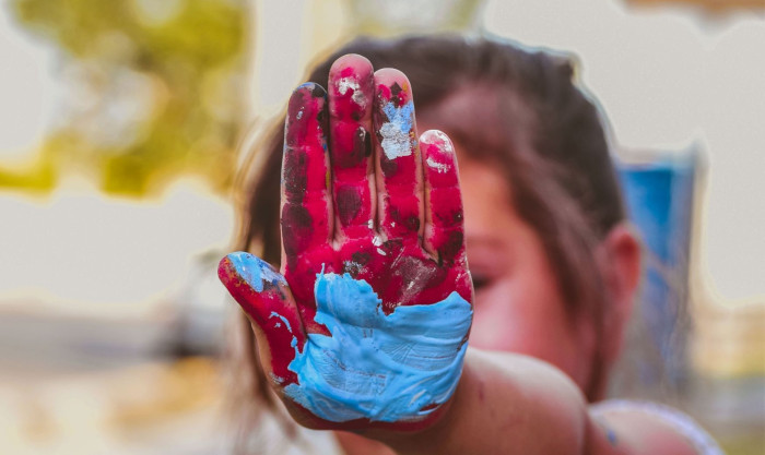 Uma criança estende a mão pintada com tintas vermelha e azul. Foto: Acervo Canva