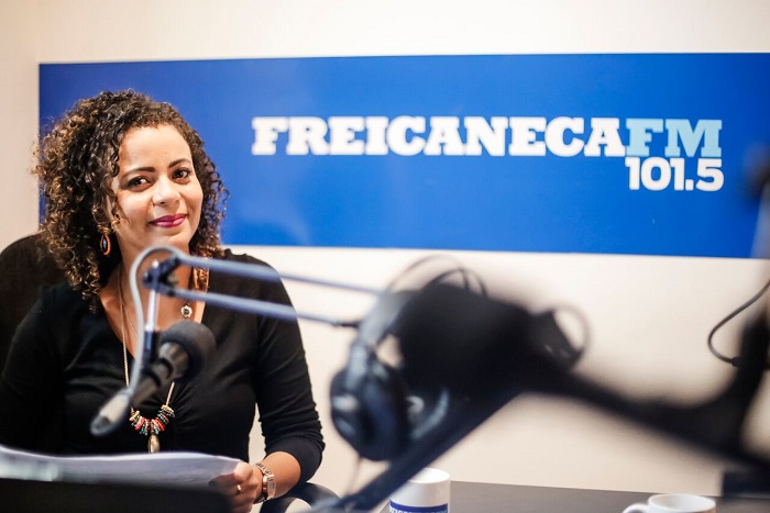 Apresentadora Nice Lima, sorrindo, no estúdio da Frei Caneca FM.