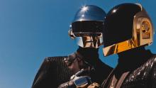 Na imagem, a dupla francesa Daft Punk, tradionalmente vestindo ternos e usando capacetes espaciais na cor prata e dourada.